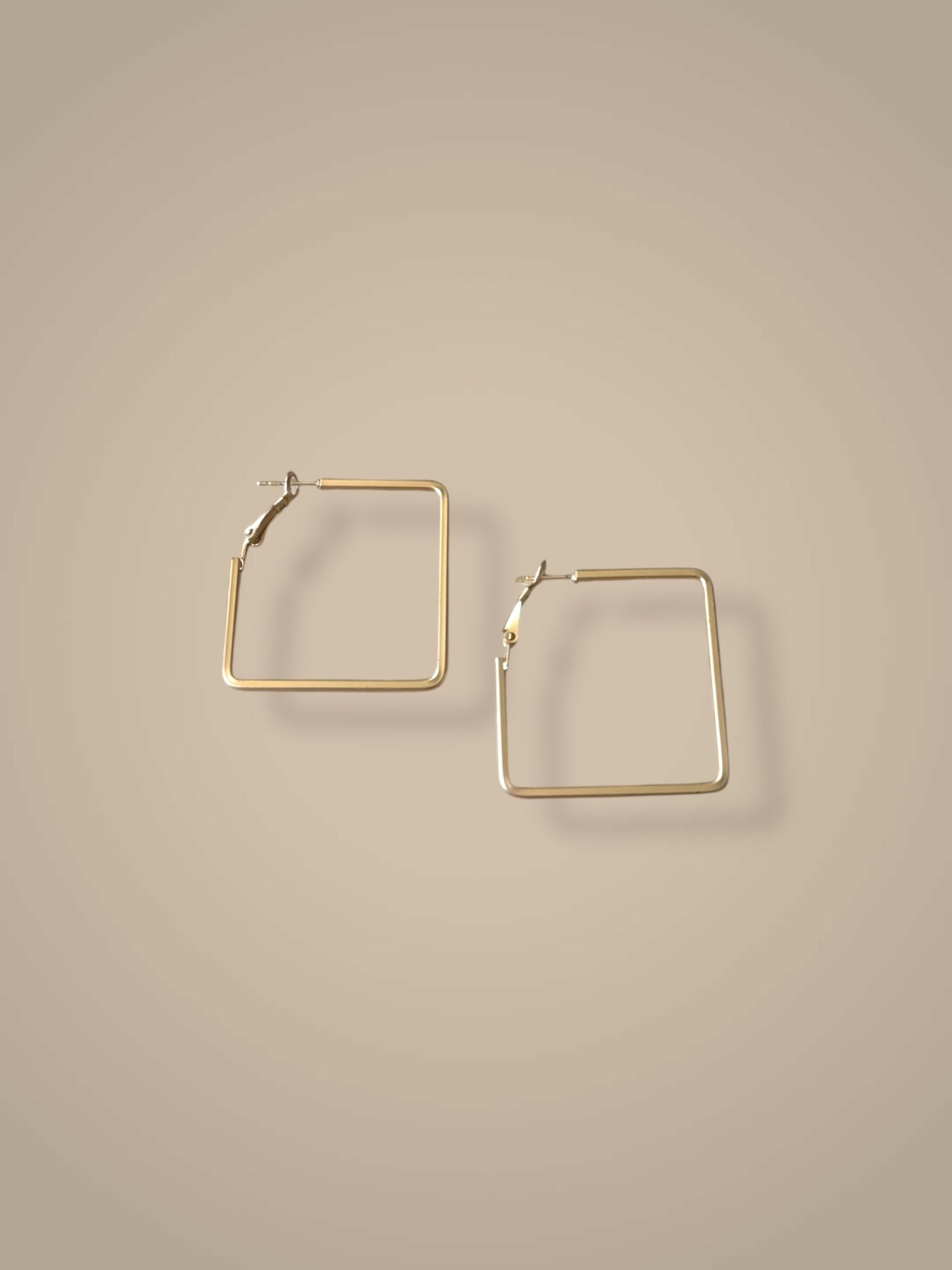Gold square hoop earrings on a beige background