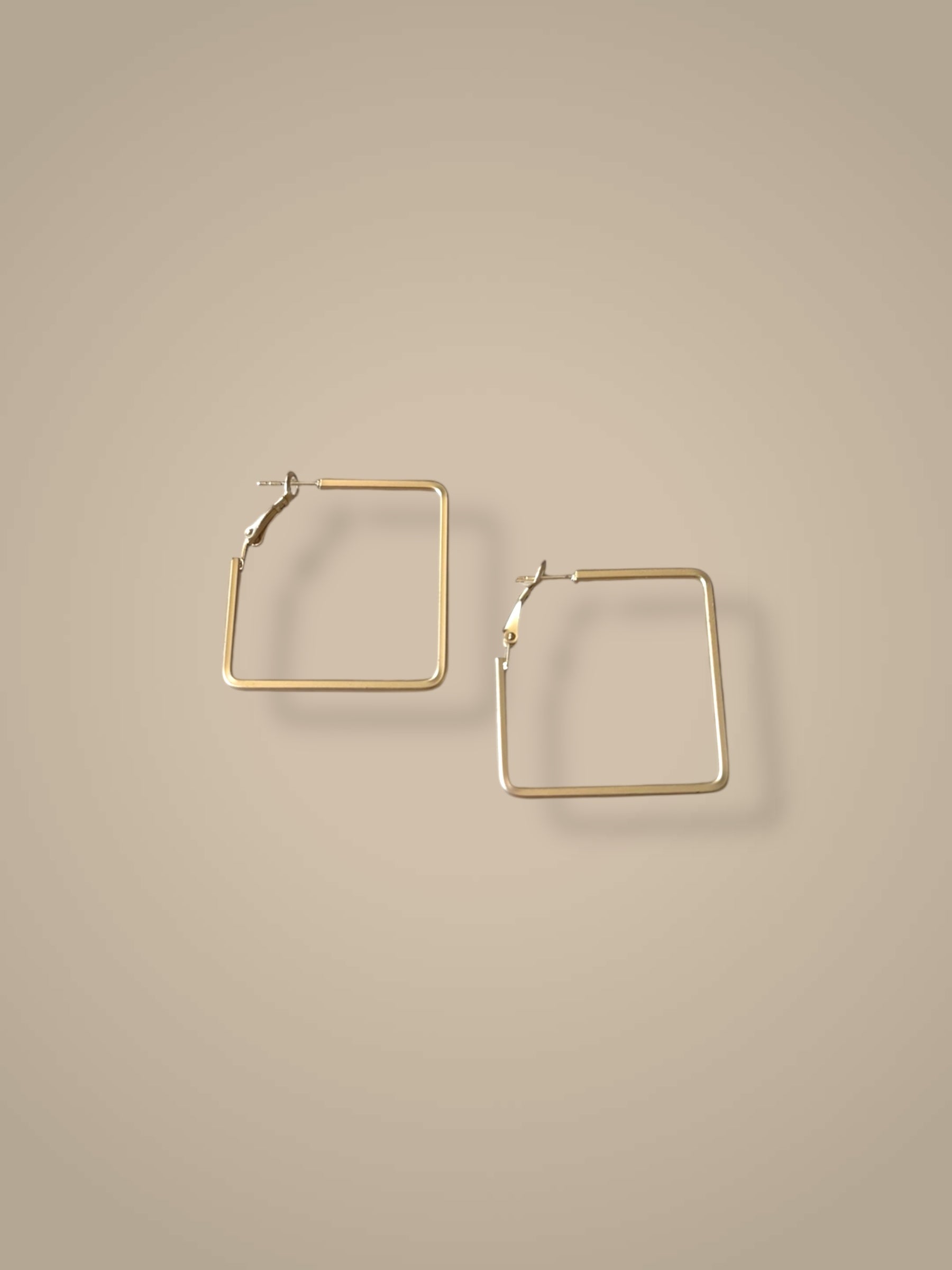 Gold square hoop earrings on a beige background